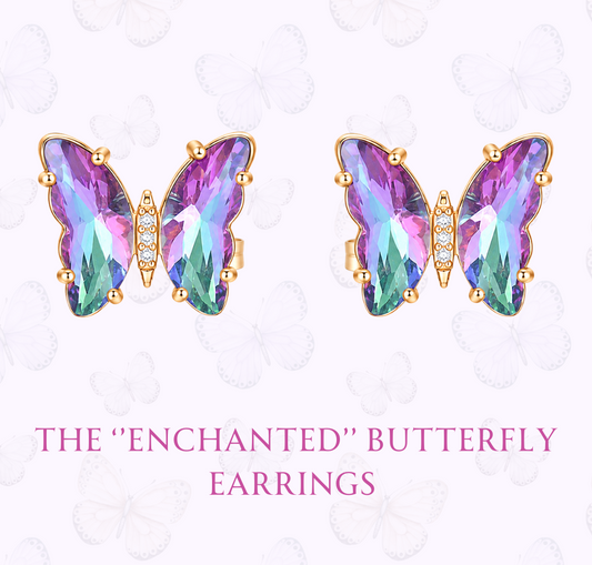 A pair of butterfly-shaped stud earrings with iridescent purple, pink, and green faceted stones in gold settings, shown on a pale pink background with decorative butterfly outlines and the text 'THE "ENCHANTED" BUTTERFLY EARRINGS' and 'www.hebejewel.