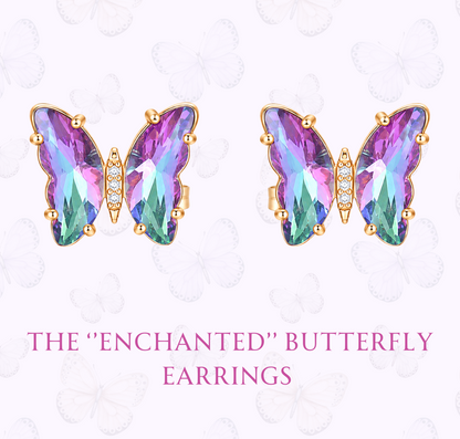 A pair of butterfly-shaped stud earrings with iridescent purple, pink, and green faceted stones in gold settings, shown on a pale pink background with decorative butterfly outlines and the text 'THE "ENCHANTED" BUTTERFLY EARRINGS' and 'www.hebejewel.