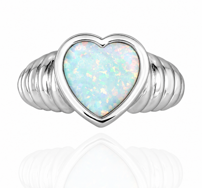 A silver ring featuring a heart-shaped opal center stone with iridescent white, blue, and pink flashes, set on a ribbed band against a white background with a soft reflection.
